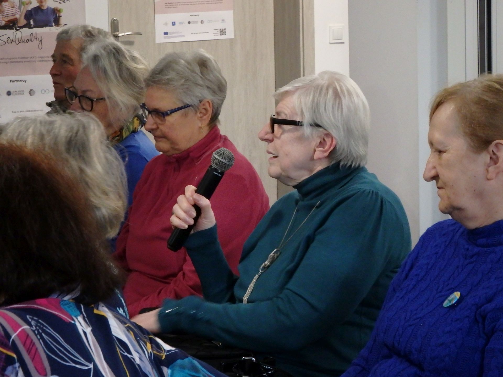Grupa Seniorow Siedziacych Podczas Seminarium Sen Quality W Tym 1 Seniorka Mowiaca Przez Mikrofon
